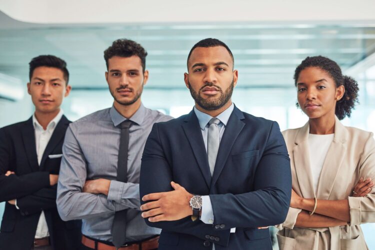 Diverse group of confident business professionals standing with arms crossed in a modern office.