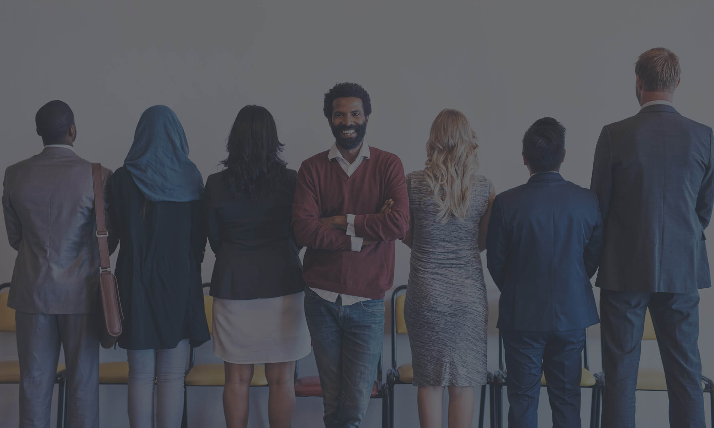 Diverse group of professionals standing in line with one person facing camera smiling confidently with a dark tint overlay