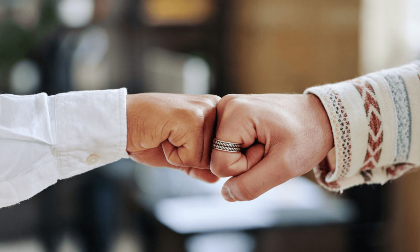 Two people fist bumping in agreement, one wearing a white shirt and one wearing a patterned sweater